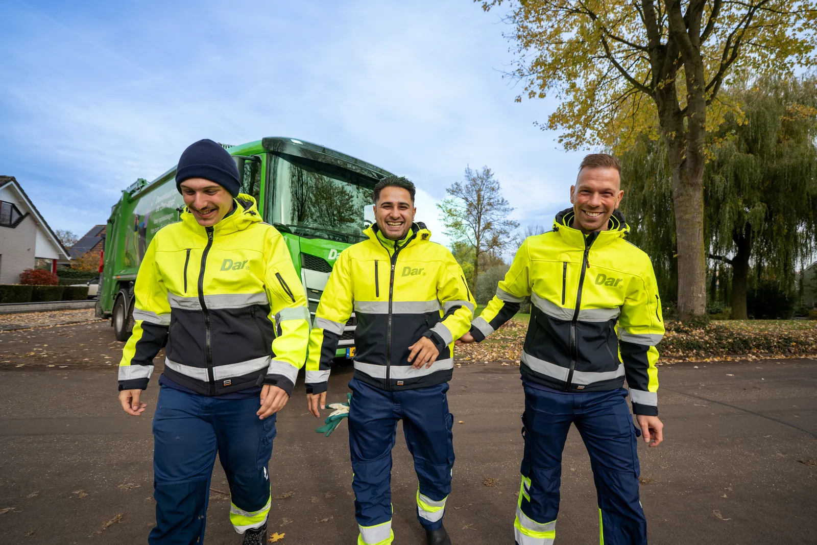 Drie medewerkers van Dar lopen lachend voor hun wagen
