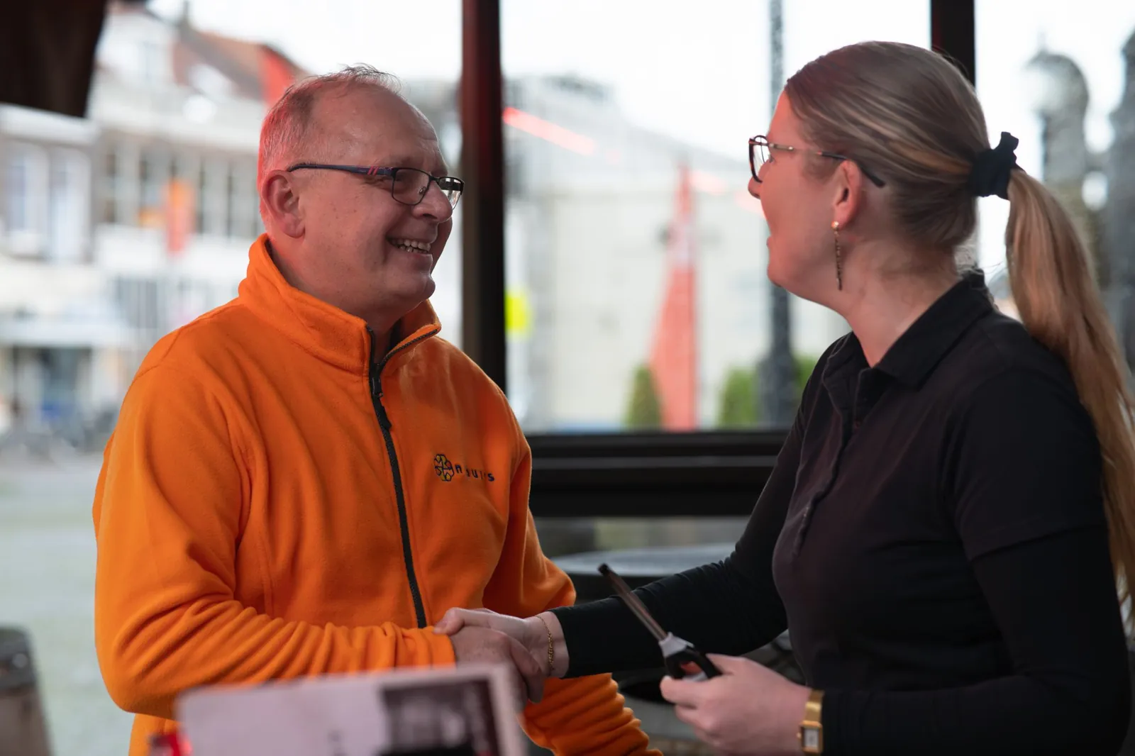 Chauffeur van Nabuurs geeft een horecaondernemer een hand aan tafel