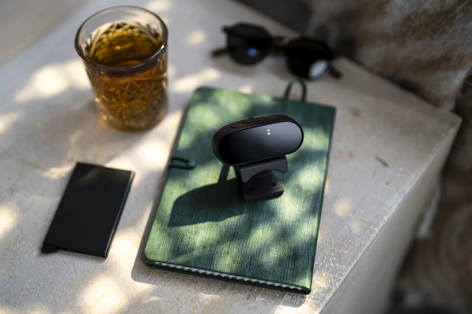 De SunBooster op een groen notitieboek in de zon, met een glas thee en een zonnebril ernaast