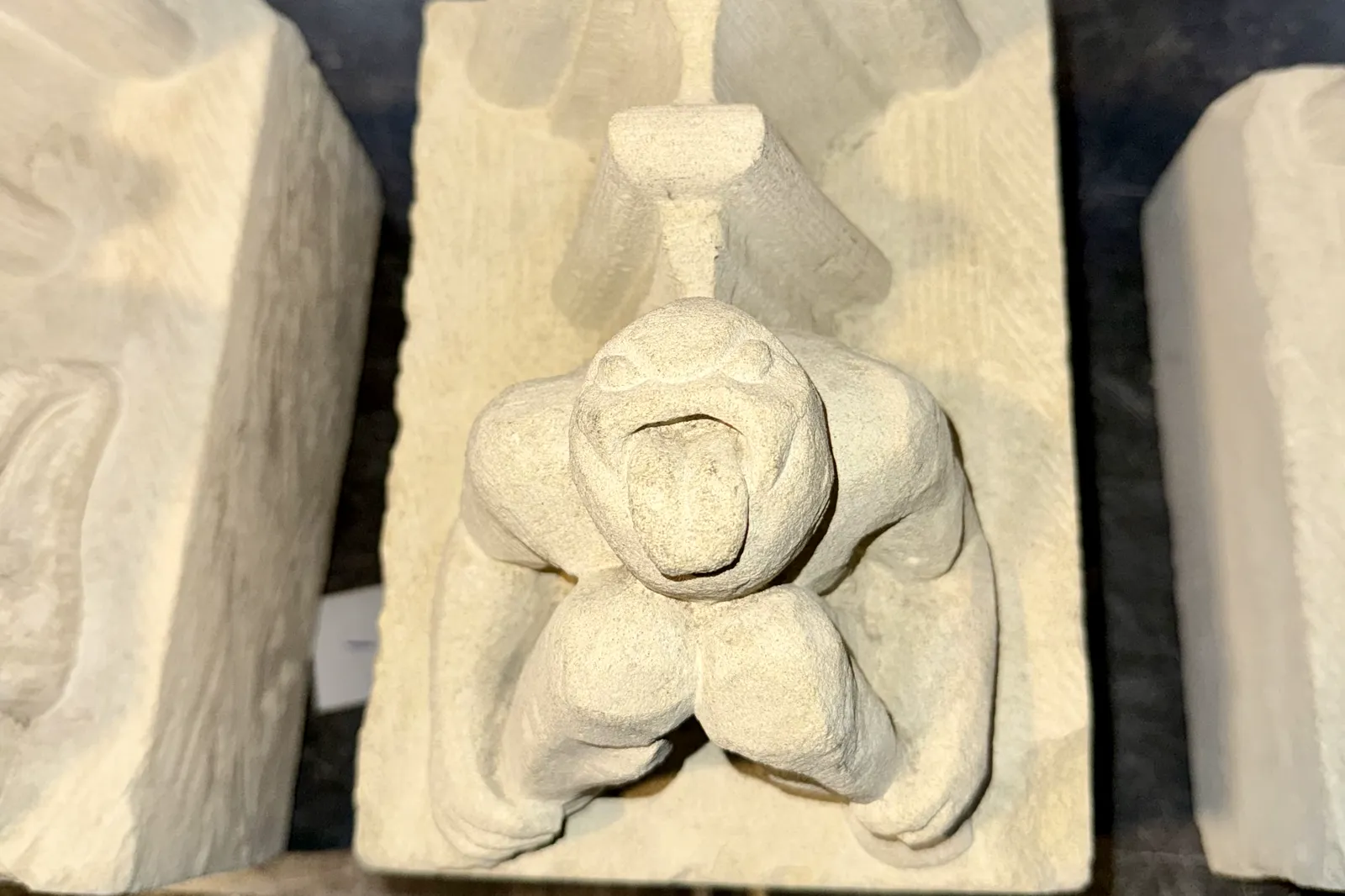Een gebeeldhouwde kraagsteen: een figuurtje met open mond dat op zijn knieën steunt, tussen twee andere stenen