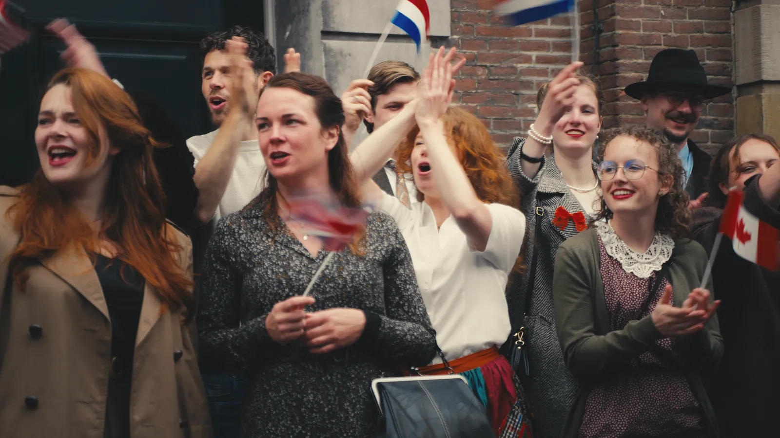 Vrouwen in kleding uit de jaren veertig juichen en zwaaien met Nederlandse en Canadese vlaggetjes langs de straat